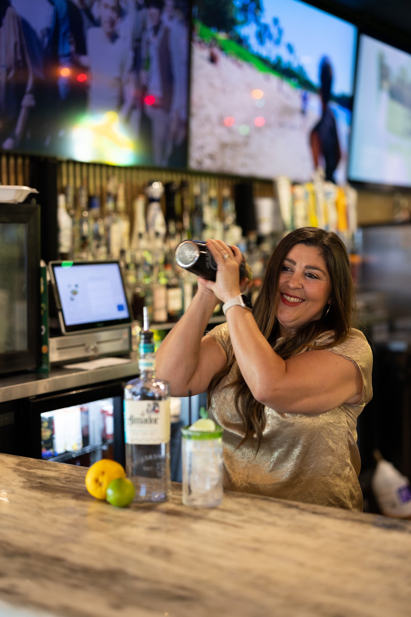 A smiling bartender shaking a cocktail behind the bar at Iguana Joe’s
